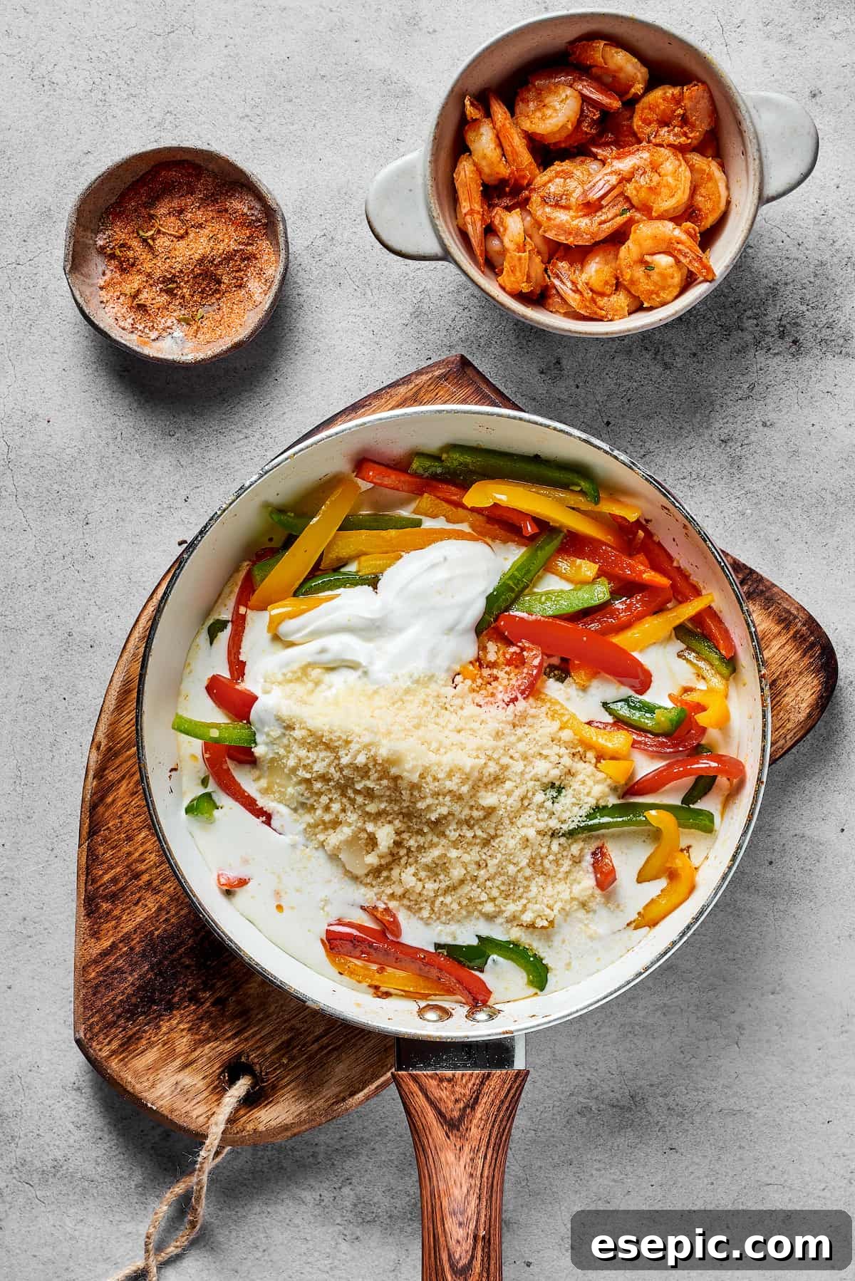 Bell peppers, parmesan, heavy cream, and cream cheese being stirred together in a skillet, forming the creamy sauce.