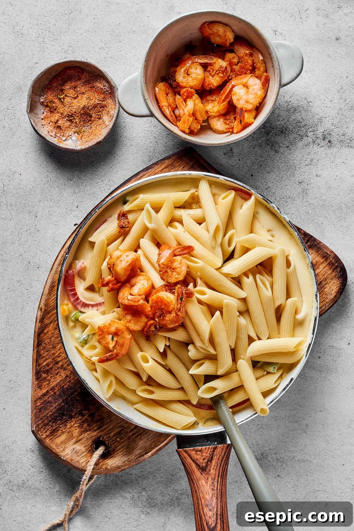 Cooked penne pasta and seasoned shrimp being mixed into the creamy bell pepper sauce in a large skillet to complete the Rasta Pasta dish.