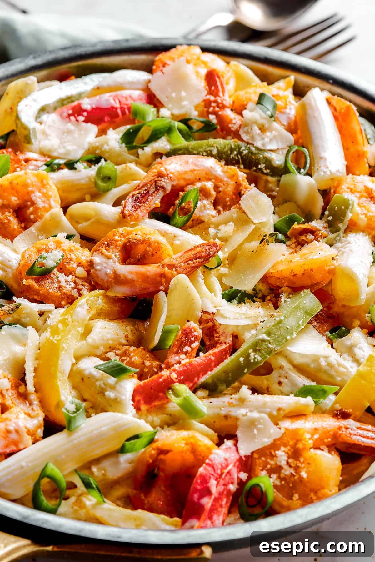 A close-up shot of a skillet brimming with creamy Rasta Pasta, featuring colorful bell peppers, tender shrimp, and penne pasta, all coated in a rich, spicy sauce.
