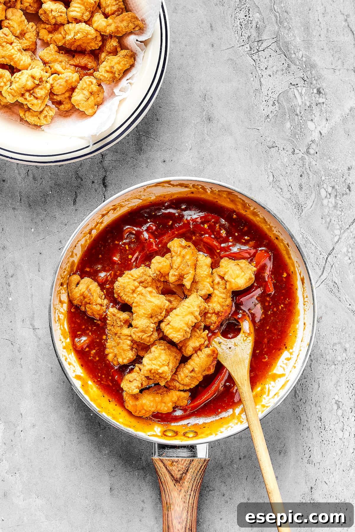 Fried chicken being tossed in a reddish sauce with bell peppers.