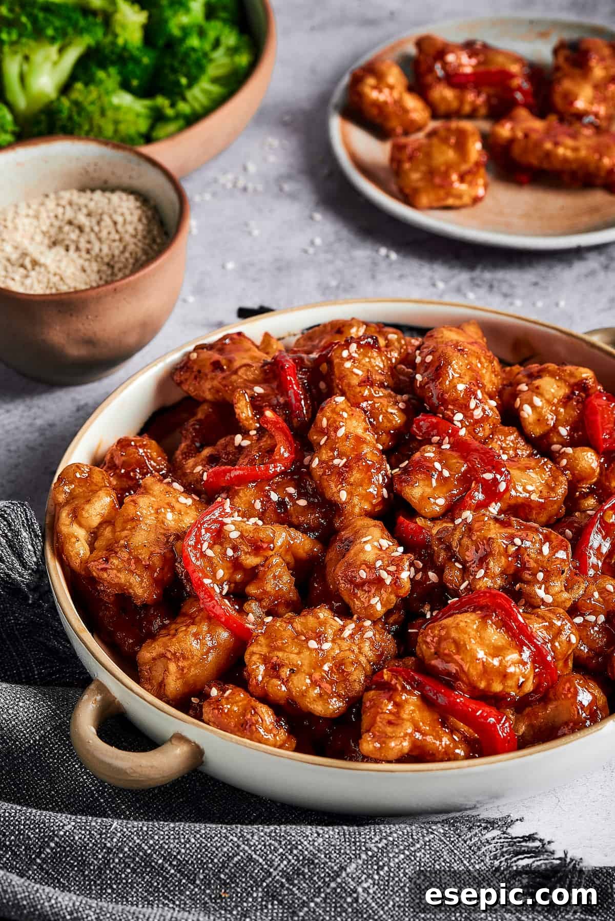 General Tso's chicken with bell peppers in a serving dish, next to dishes of broccoli and other ingredients.