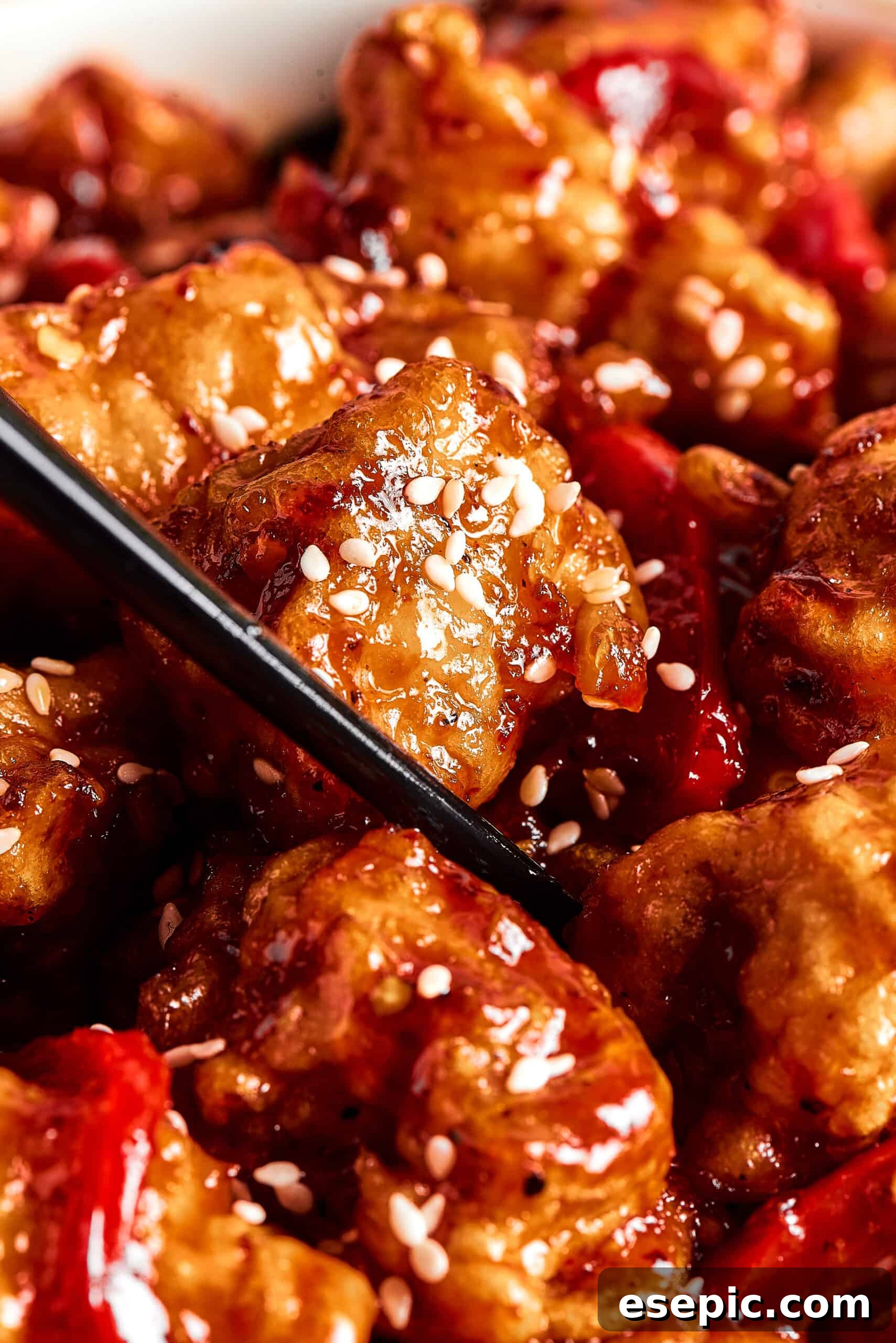 A pair of chopsticks picking up a piece of sticky chicken from a dish.