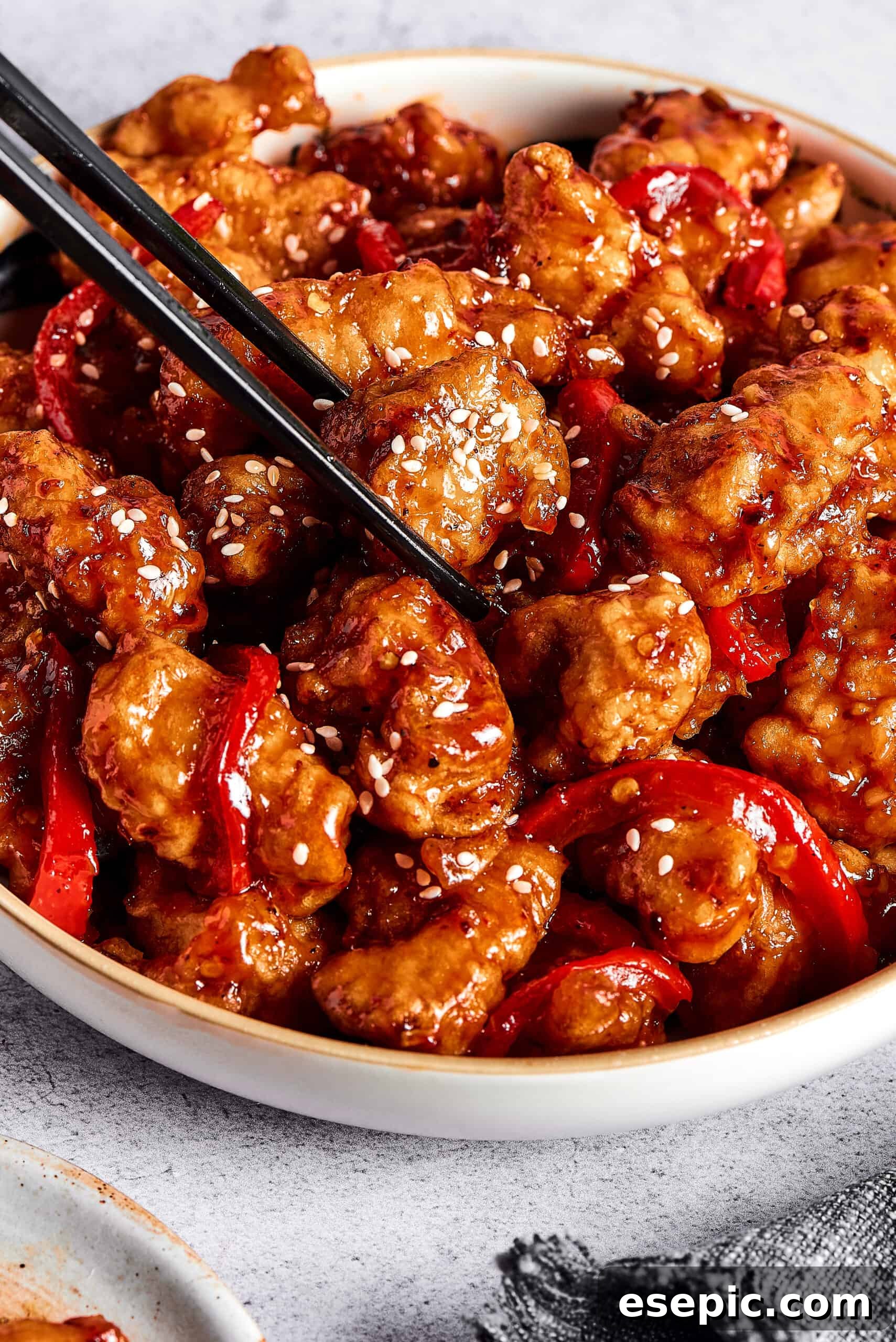 A pair of chopsticks picking up a piece of sticky chicken from a dish.