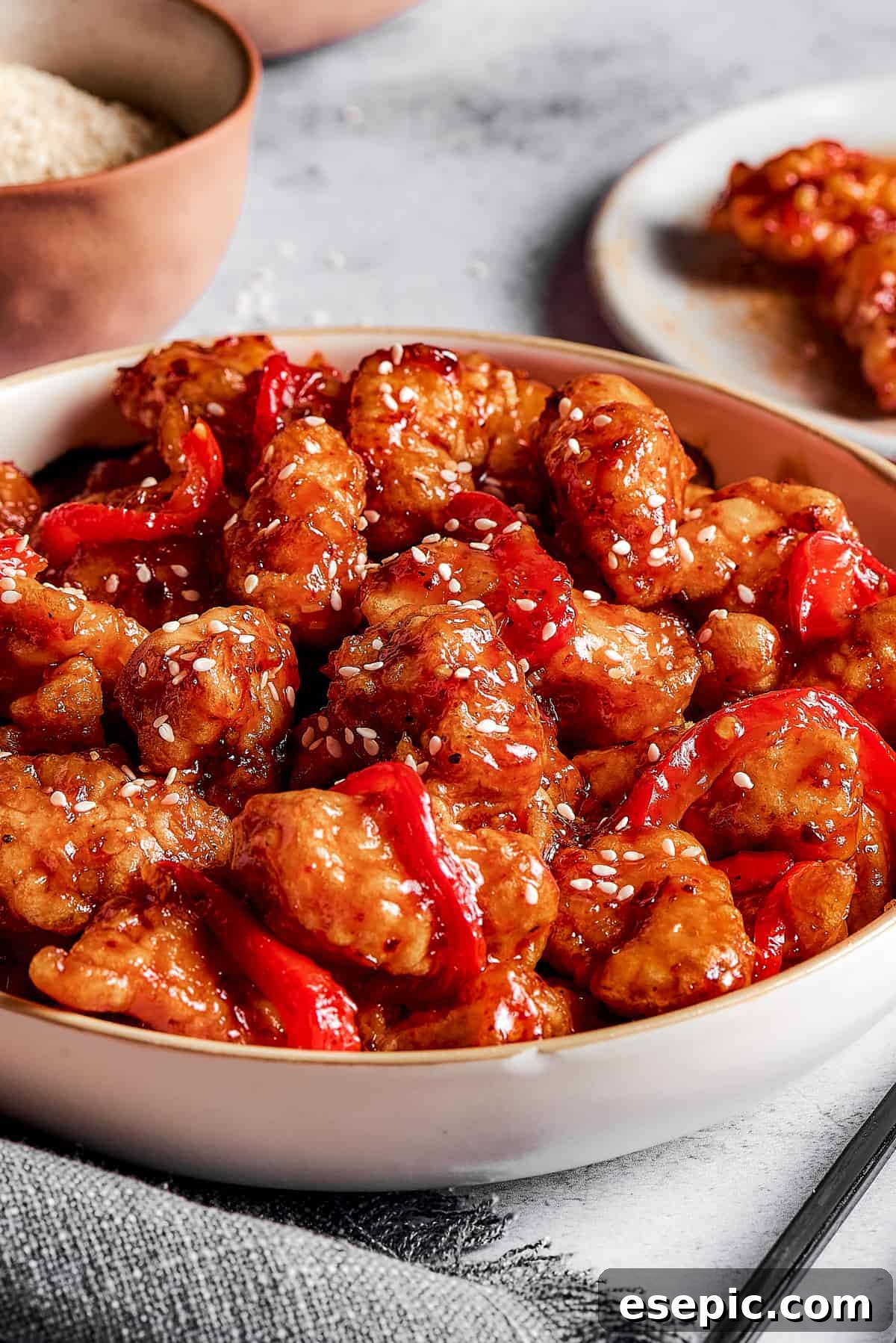 General Tso's chicken with bell peppers in a serving dish, next to dishes of broccoli and other ingredients.
