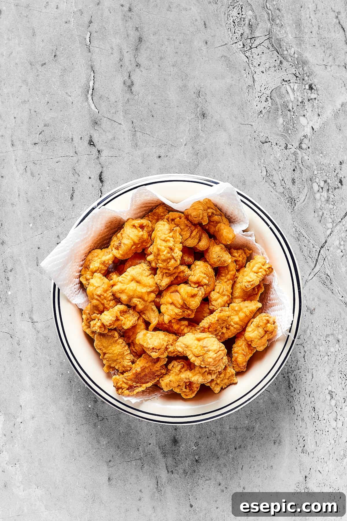 Fried chicken pieces draining on a paper-towel-lined platter.