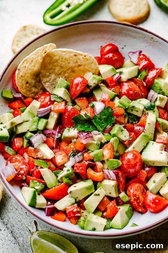 A bowl filled with chopped tomatoes and avocado, surrounded by tortilla chips, highlighting the fresh ingredients of the salsa.