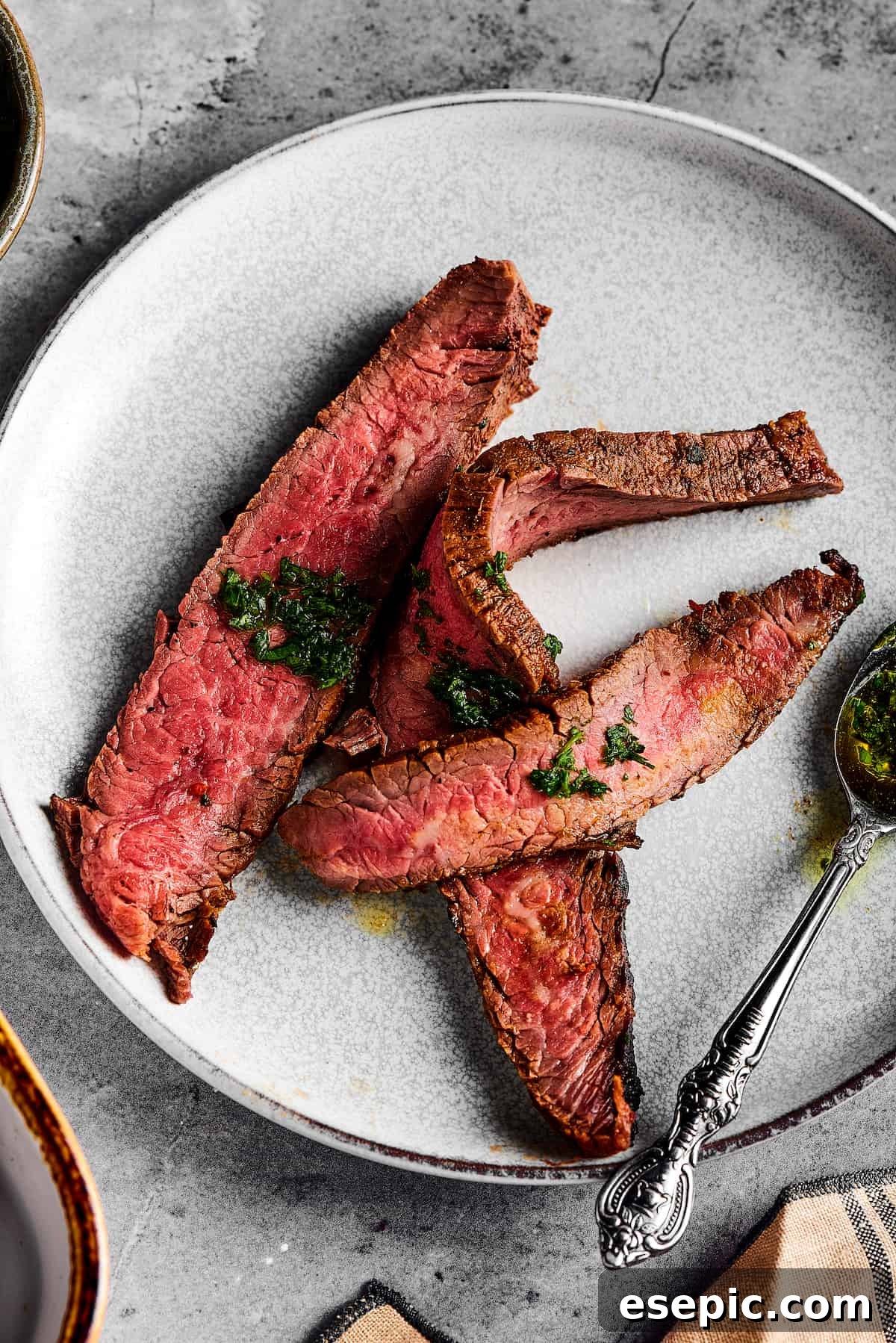 Orange and lime juice, garlic and jalapeno, maple and cumin - this easy Grilled Carne Asada is drenched in a medley of mouthwatering flavors! Medium-rare steak slices on a small white plate, artfully drizzled with a light green sauce, highlighting its juicy interior.