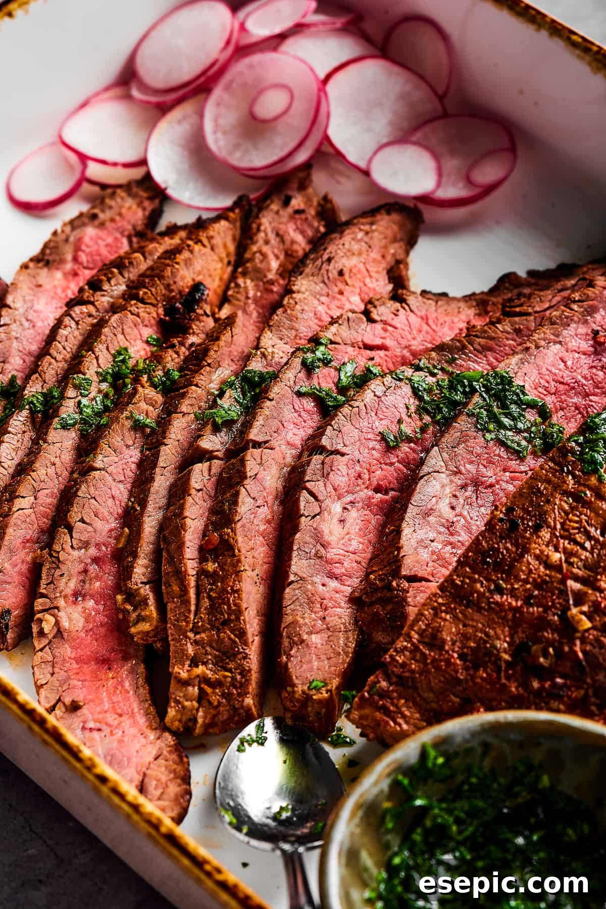 Orange and lime juice, garlic and jalapeno, maple and cumin - this easy Grilled Carne Asada is drenched in a medley of mouthwatering flavors! Slices of grilled flank steak next to a small cup of vibrant green herb sauce.