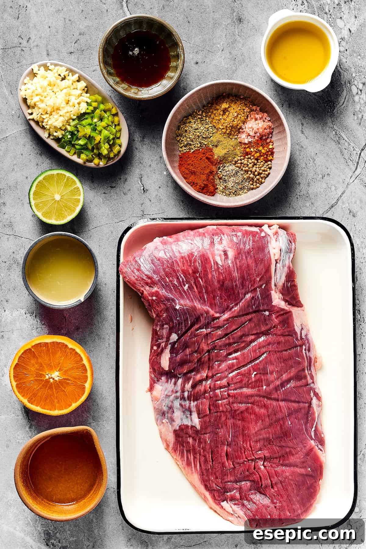 Orange and lime juice, garlic and jalapeno, jalapeno, maple and cumin - this easy Grilled Carne Asada is drenched in a medley of mouthwatering flavors! Various ingredients for the marinade laid out: Minced garlic and jalapeno, maple syrup, assorted spices, olive oil, fresh lime juice, orange juice, and a raw flank steak.