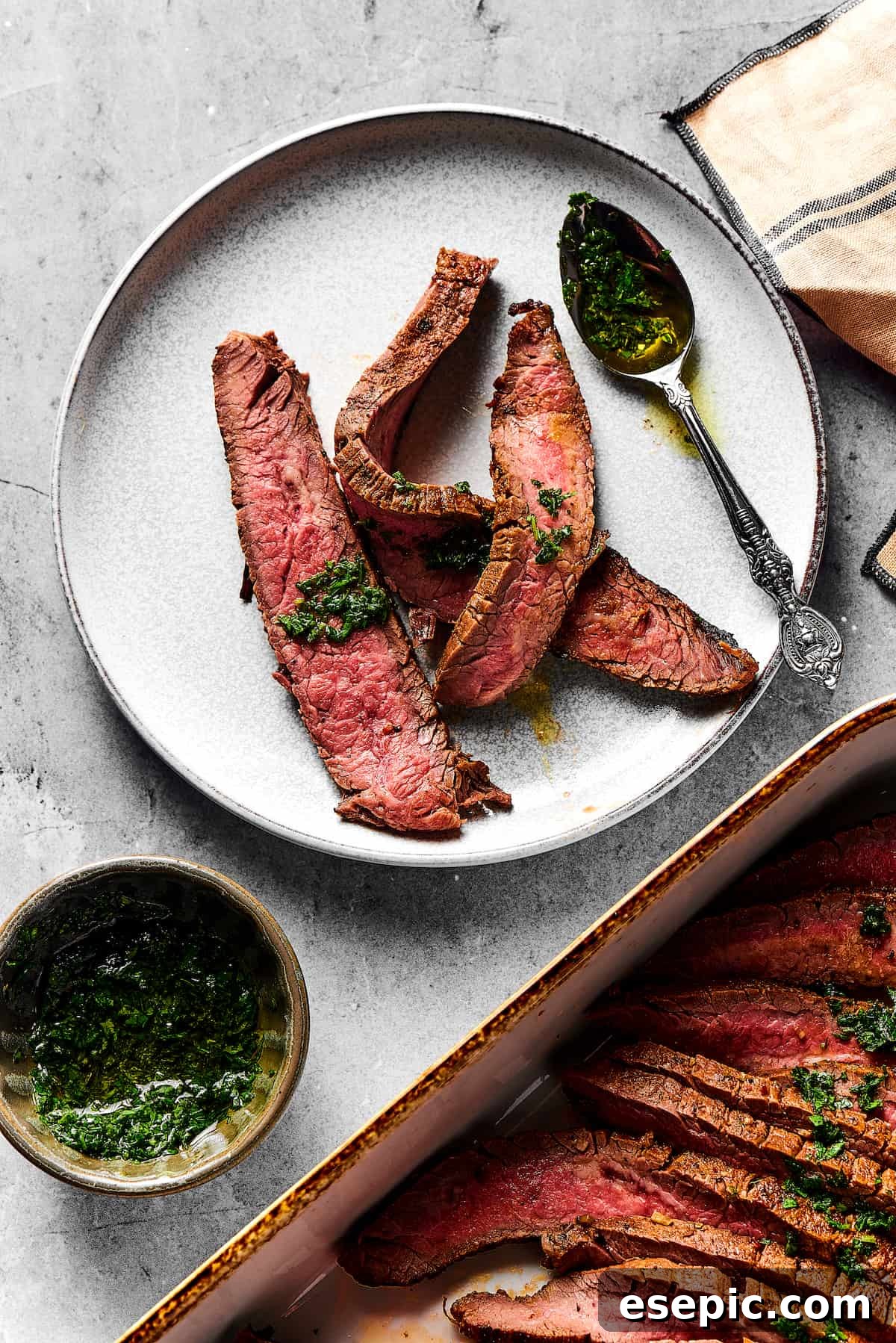 Orange and lime juice, garlic and jalapeno, maple and cumin - this easy Grilled Carne Asada is drenched in a medley of mouthwatering flavors! A small plate with three strips of medium-rare grilled carne asada on it. Nearby is a large platter of the steak slices, a cup of sauce, and a spoon, showcasing the full meal.