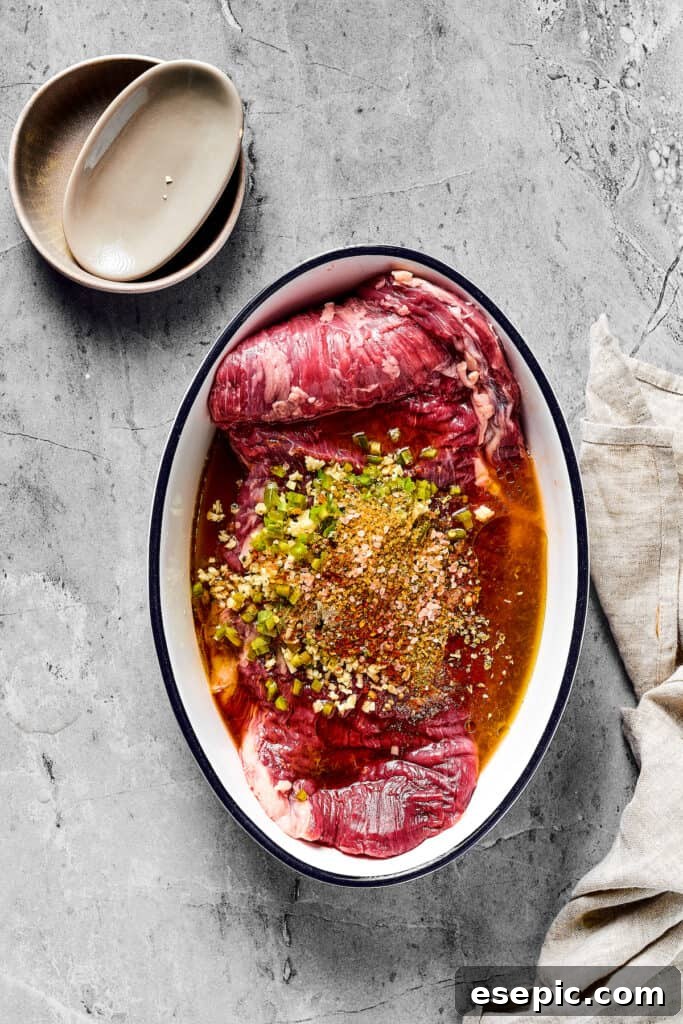Juicy Grilled Carne Asada Perfection 2 A flank steak submerged in a rich, vibrant marinade within an enamel oval dish.