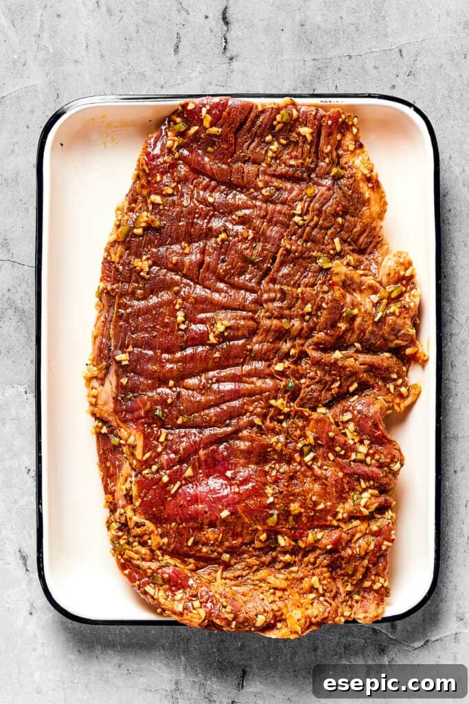 Juicy Grilled Carne Asada Perfection 4 Raw, marinated flank steak resting on an enamel tray, ready for grilling.