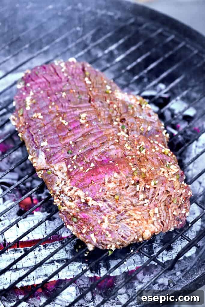 Juicy Grilled Carne Asada Perfection 5 A marinated flank steak searing on a hot charcoal grill, smoke rising.