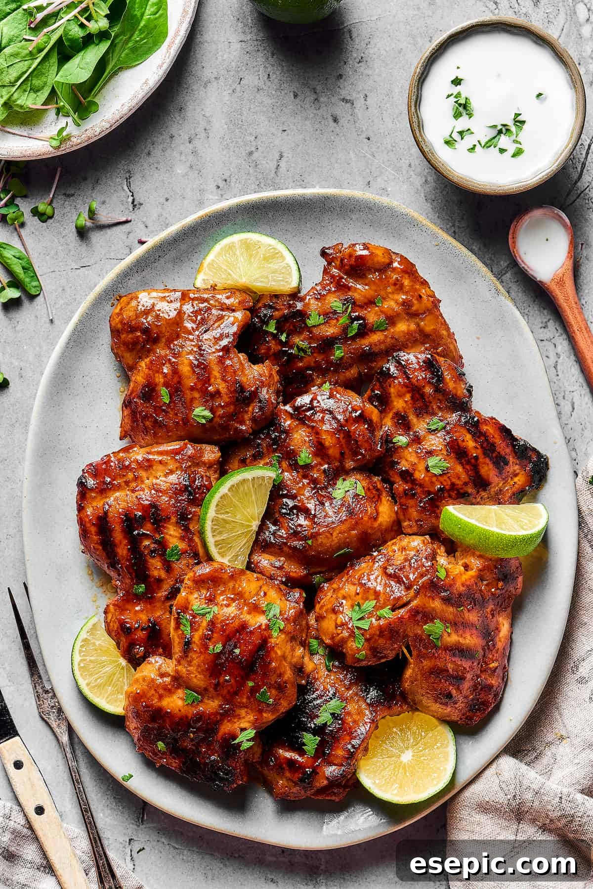 An oval platter of grilled chicken thighs, garnished with parsley and lime wedges.