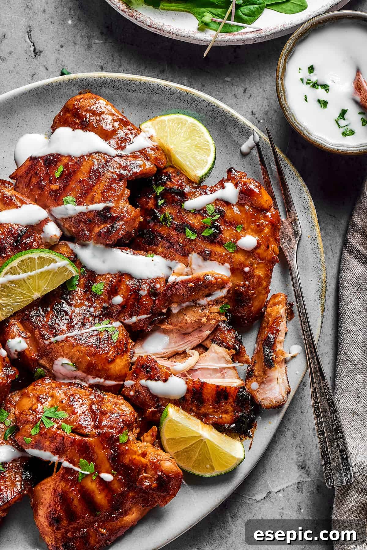 A serving dish of chicken thighs, grilled and garnished with a drizzle of yogurt.