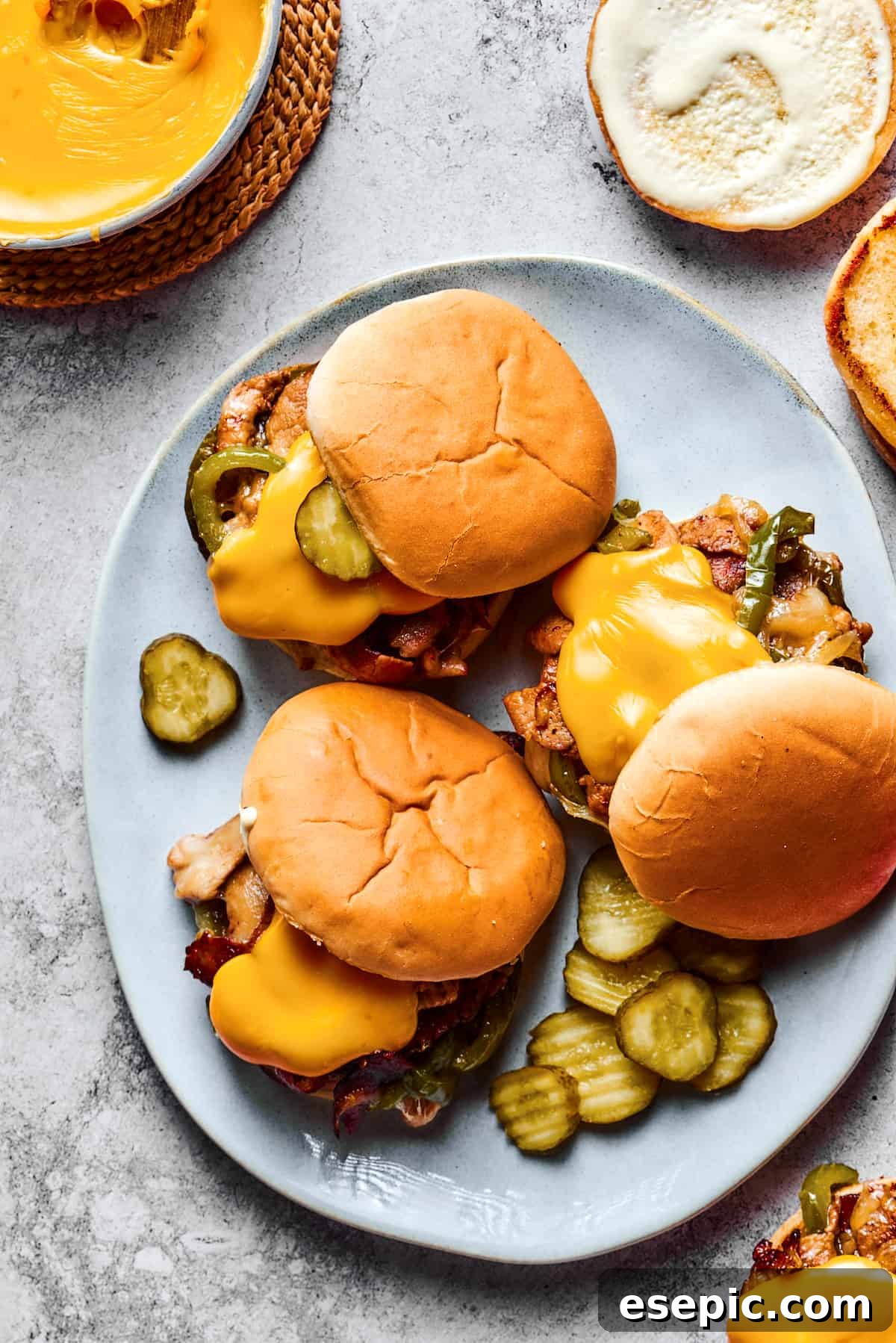 Overhead shot of a large platter. Three sandwiches are on the platter, each one piled high with philly cheesesteak fillings and garnished with pickles.