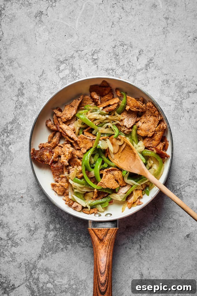 Sliced steak, onion, and bell pepper cooking in a skillet.