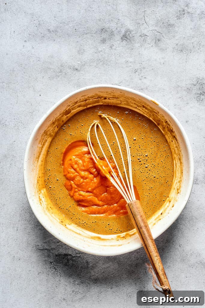 Decadent Pumpkin Cheesecake Muffins 2 A close-up of wet muffin batter ingredients in a mixing bowl with a whisk, showing the vibrant orange pumpkin puree blended with other liquids.