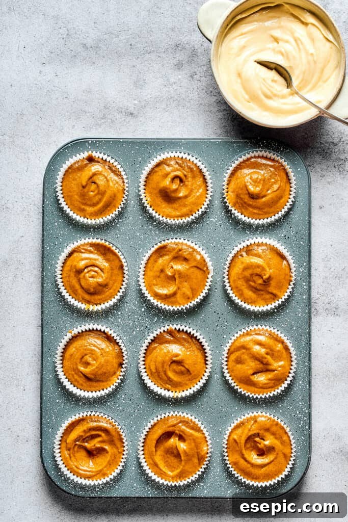Decadent Pumpkin Cheesecake Muffins 5 A muffin tin with pumpkin batter poured into paper liners, ready for the cream cheese swirl and topping.