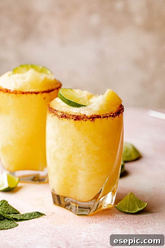 Sun-Kissed Pineapple Margaritas 6 Two glasses of frozen pineapple margaritas with a chili salt rim garnished with lime and mint, inviting guests to enjoy.