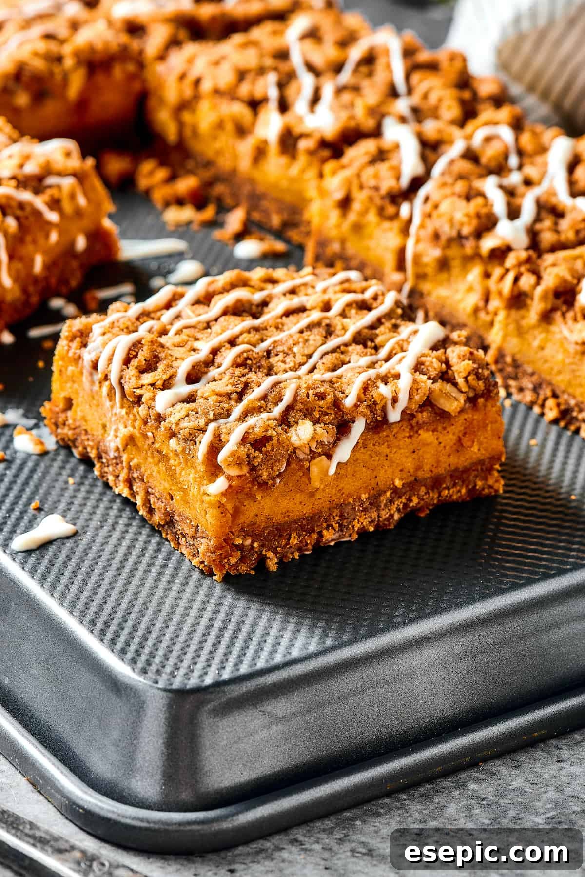 Pumpkin cheesecake bars drizzled with cream cheese topping, showcasing the layers.