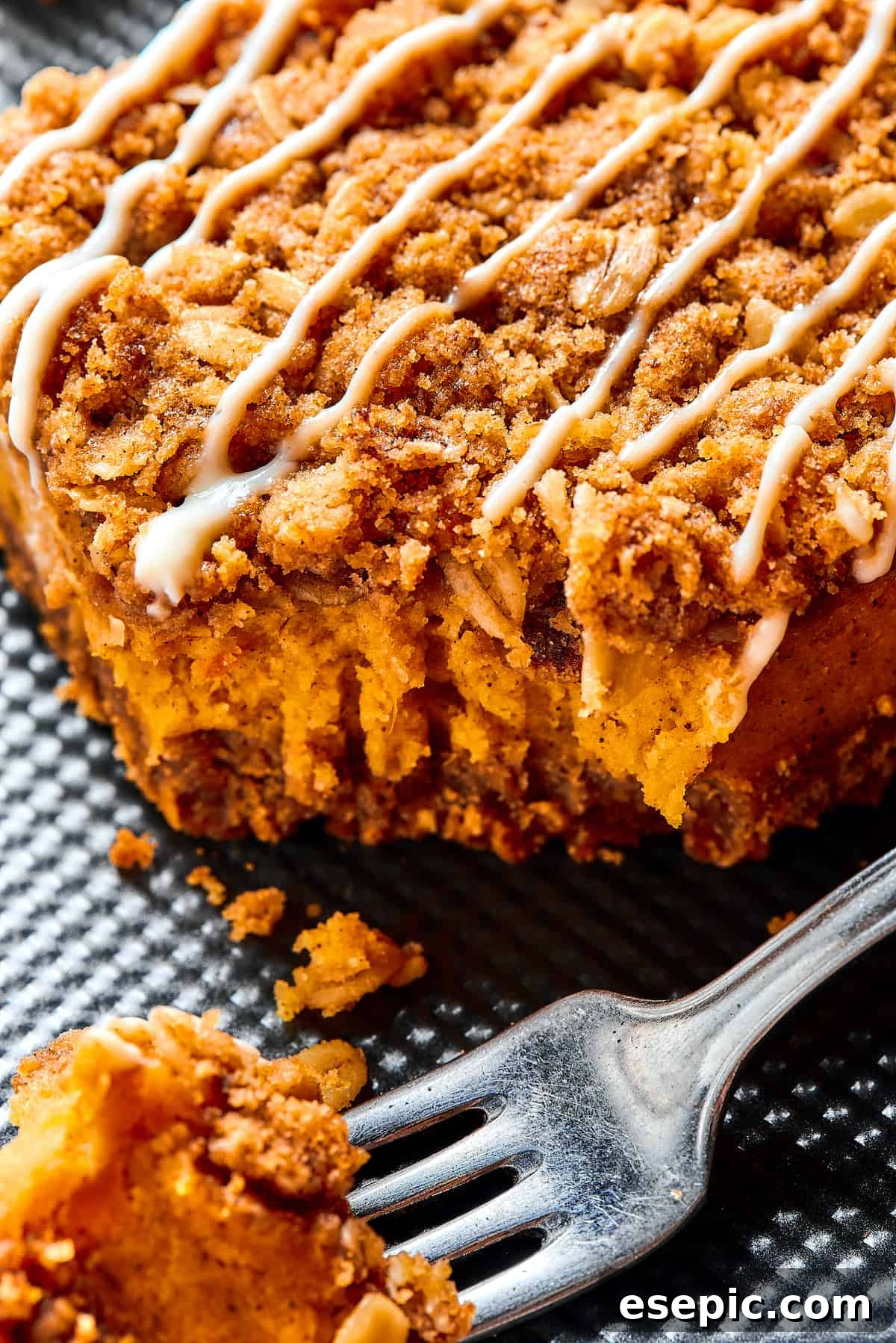 Close-up shot of a single pumpkin cheesecake bar, showing the distinct layers and crumbly streusel topping, with a fork beside it.