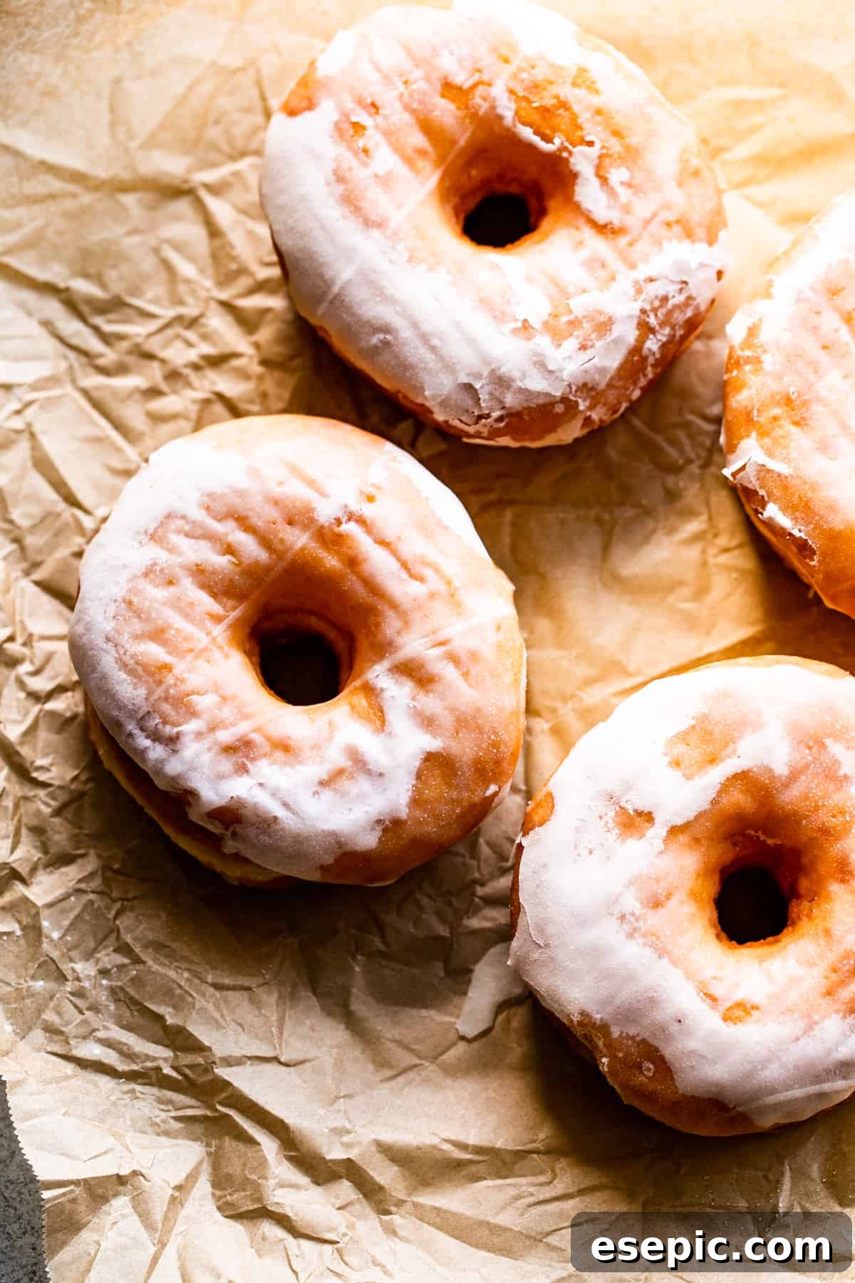 Cozy Baked Apple Cider Doughnuts with Maple Drizzle 4 three perfectly glazed apple cider doughnuts arranged on light brown baking paper, highlighting their delightful texture.