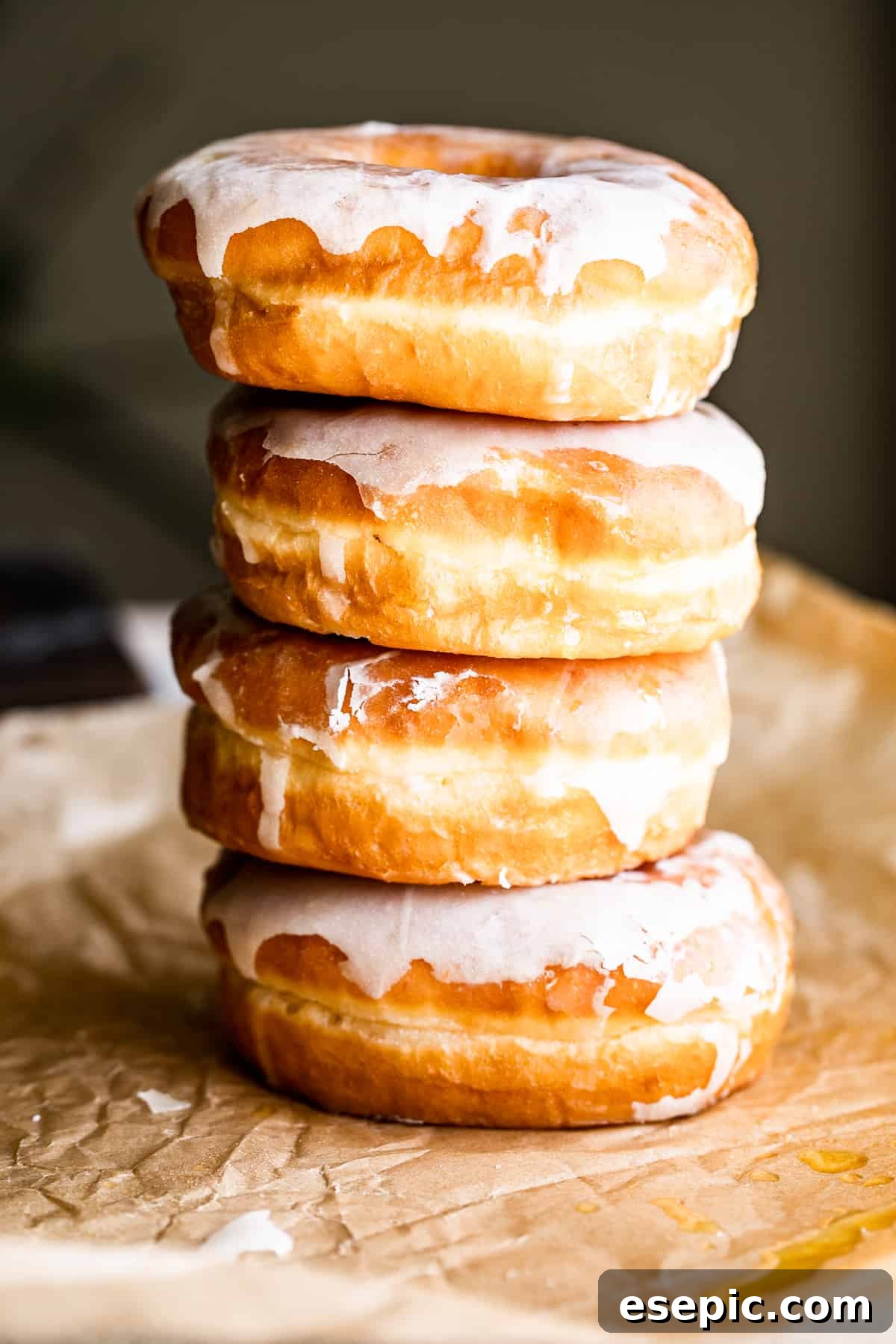 Cozy Baked Apple Cider Doughnuts with Maple Drizzle 5 four baked apple cider doughnuts stacked vertically, highlighting their golden brown color and the luscious maple glaze, against a complementary brown backdrop.
