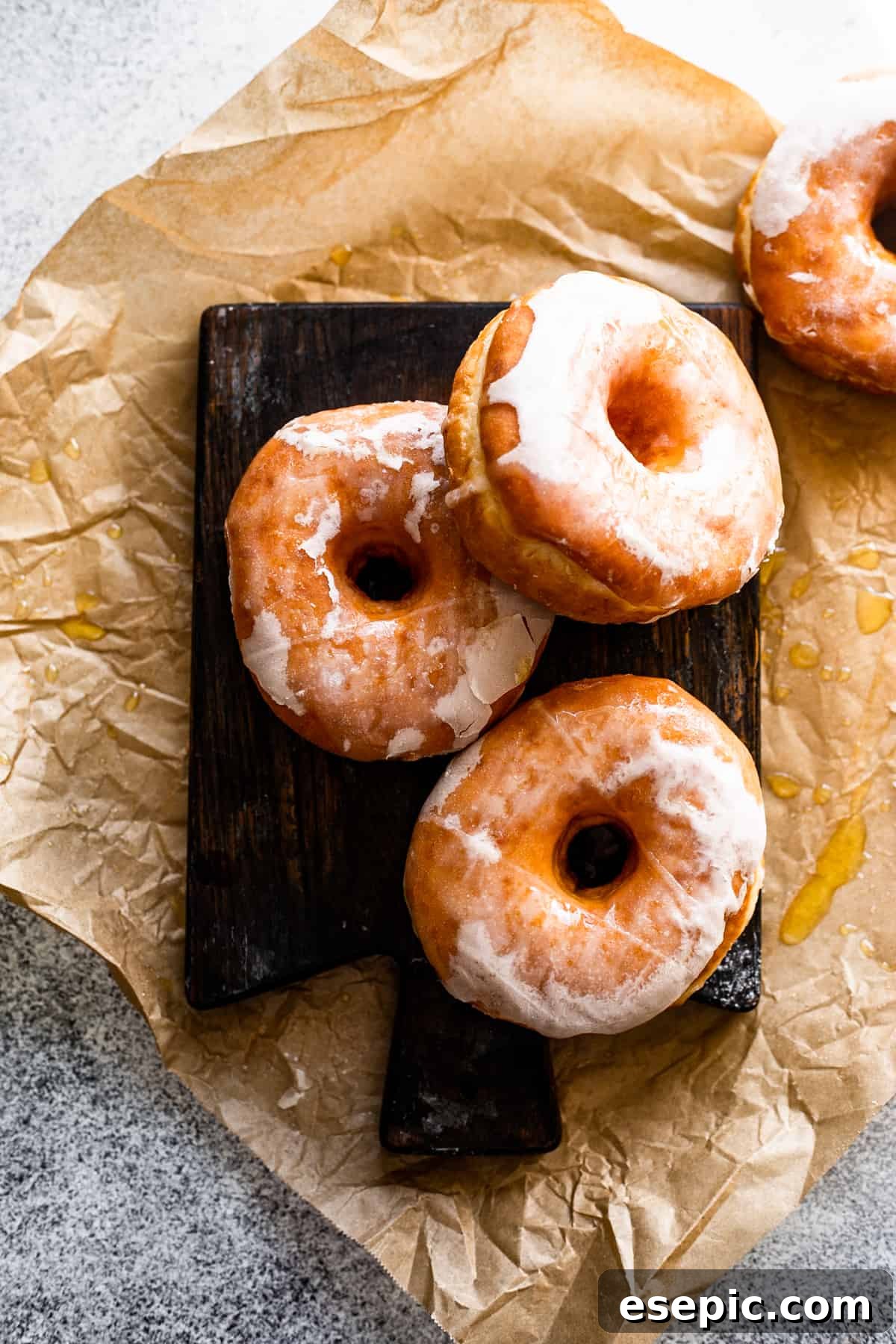 Cozy Baked Apple Cider Doughnuts with Maple Drizzle 6 overhead photo of three maple glazed apple cider doughnuts artfully arranged on a dark brown wooden board, with an additional doughnut set to the side.