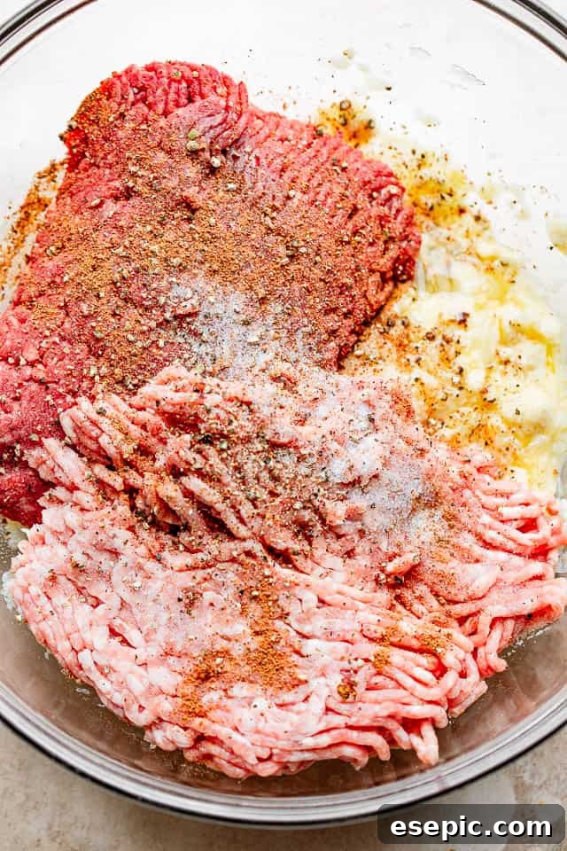 A glass bowl filled with the fresh ingredients for making homemade Swedish meatballs, including ground beef, pork, bread, milk, and spices.