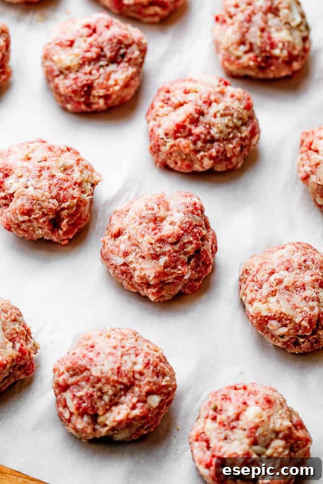 Neatly rolled meatballs arranged on white parchment paper, prepared for cooking.