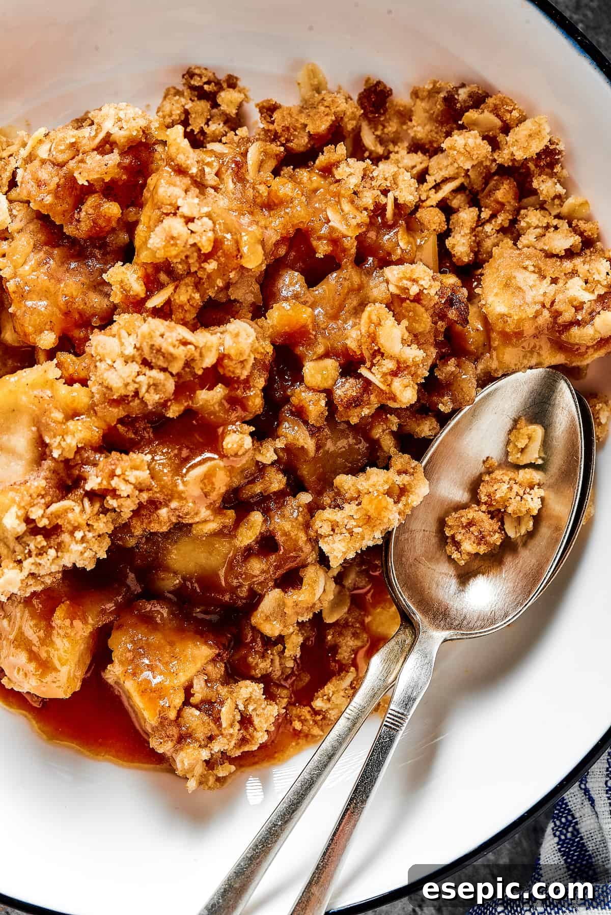 Close-up shot of apple crisp in a dessert bowl, with a spoon. A perfectly baked and ready-to-eat apple crisp.