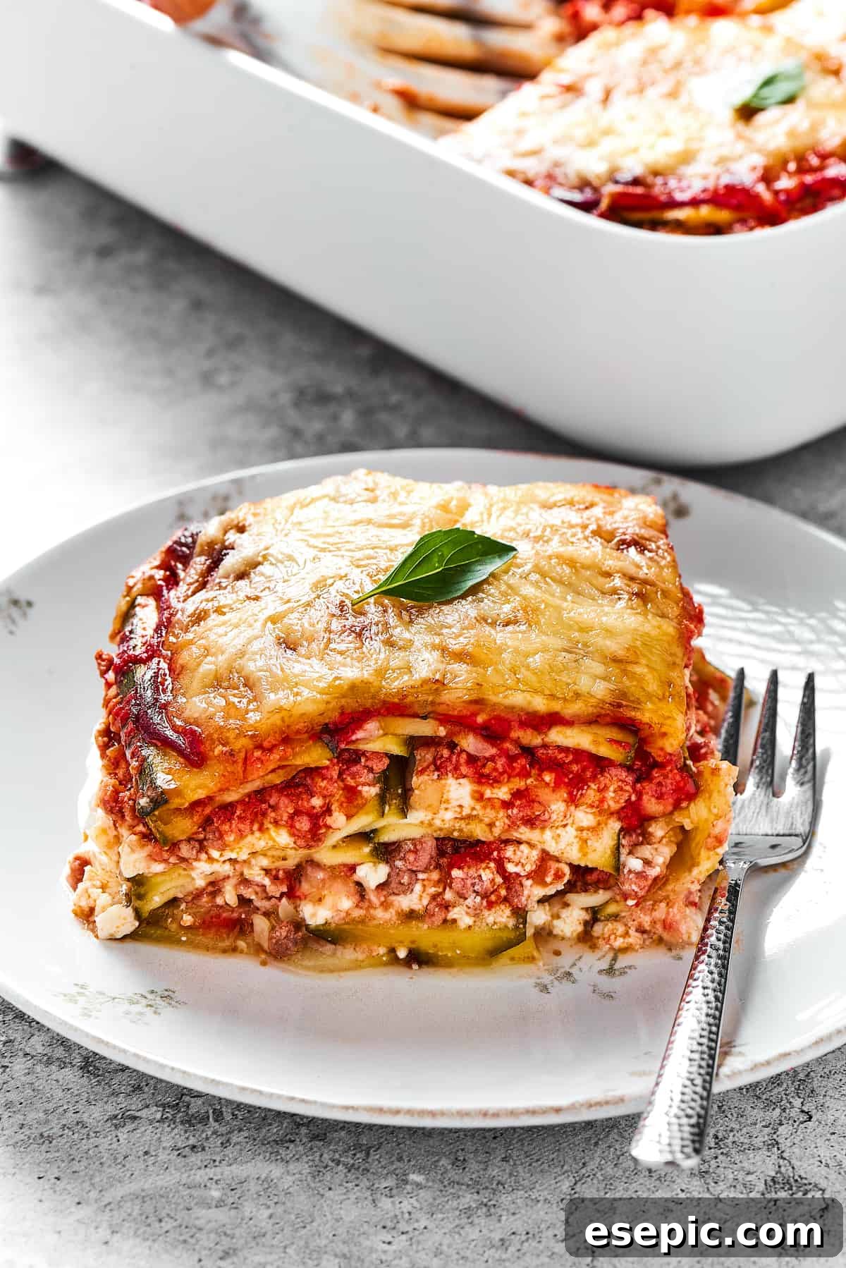Comforting Zucchini Lasagna with meat sauce is the perfect low-carb family meal. Cheesy, saucy, and healthy, with zucchini instead of pasta! A perfectly portioned square of zucchini lasagna resting on a white plate, showcasing its well-defined, delicious layers.