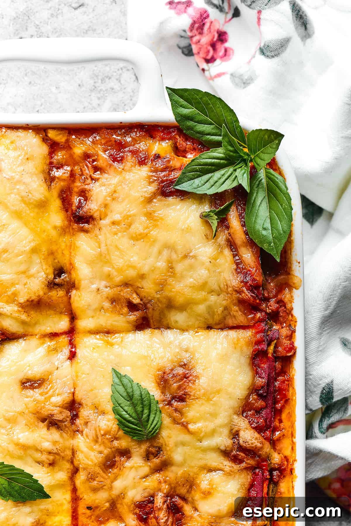 Comforting Zucchini Lasagna with meat sauce is the perfect low-carb family meal. Cheesy, saucy, and healthy, with zucchini instead of pasta! A close-up view of a corner of Zucchini Lasagna, beautifully garnished with vibrant fresh basil leaves, showcasing its rich layers.