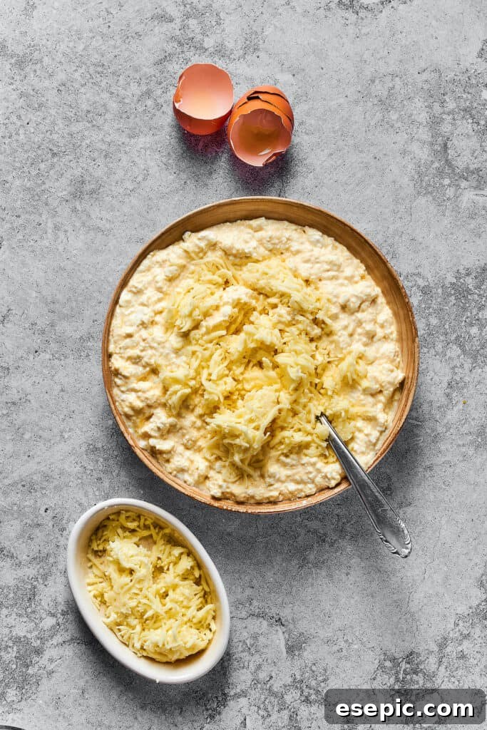 Shredded mozzarella being added to a large bowl containing the cottage cheese, eggs, and Parmesan mixture for the lasagna filling.