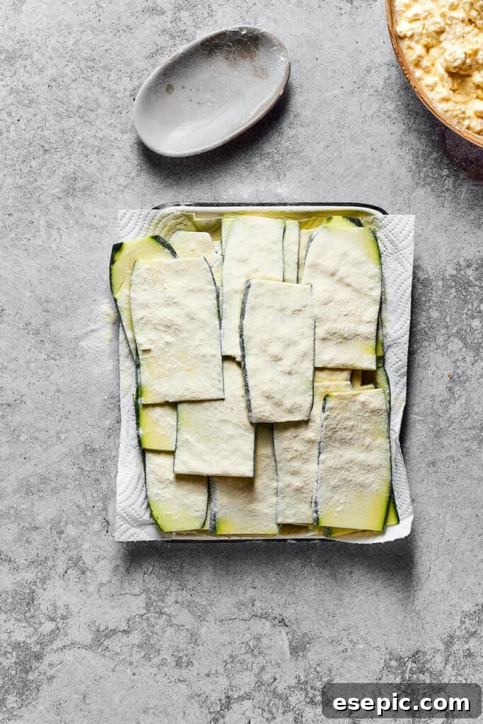 Strips of raw zucchini, lightly floured and resting on a paper-towel-lined tray after being salted and drained, ready for layering.