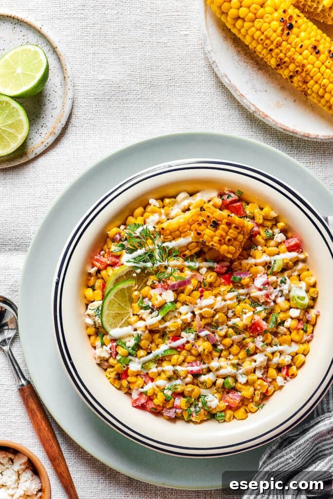 Creamy Mexican Street Corn Salad 5 Mexican street corn asalad in a serving bowl, garnished with dressing and lime wedges.