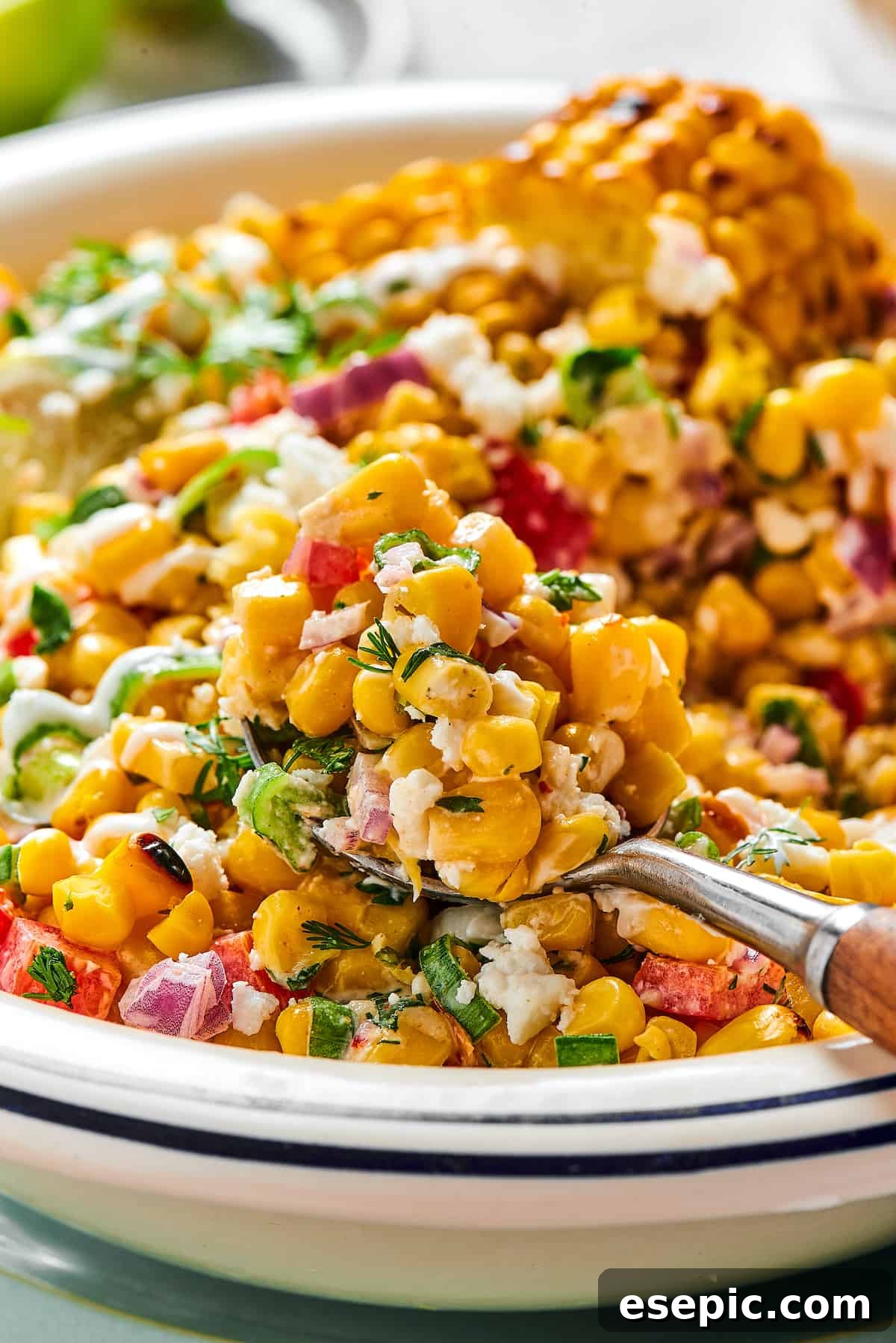 Mexican Street Corn Salad is a mouthwatering dish that’ll have everyone begging for the recipe! Fresh corn kernels in a killer creamy sauce. A spoonful of grilled corn salad being lifted toward the camera from a serving dish.