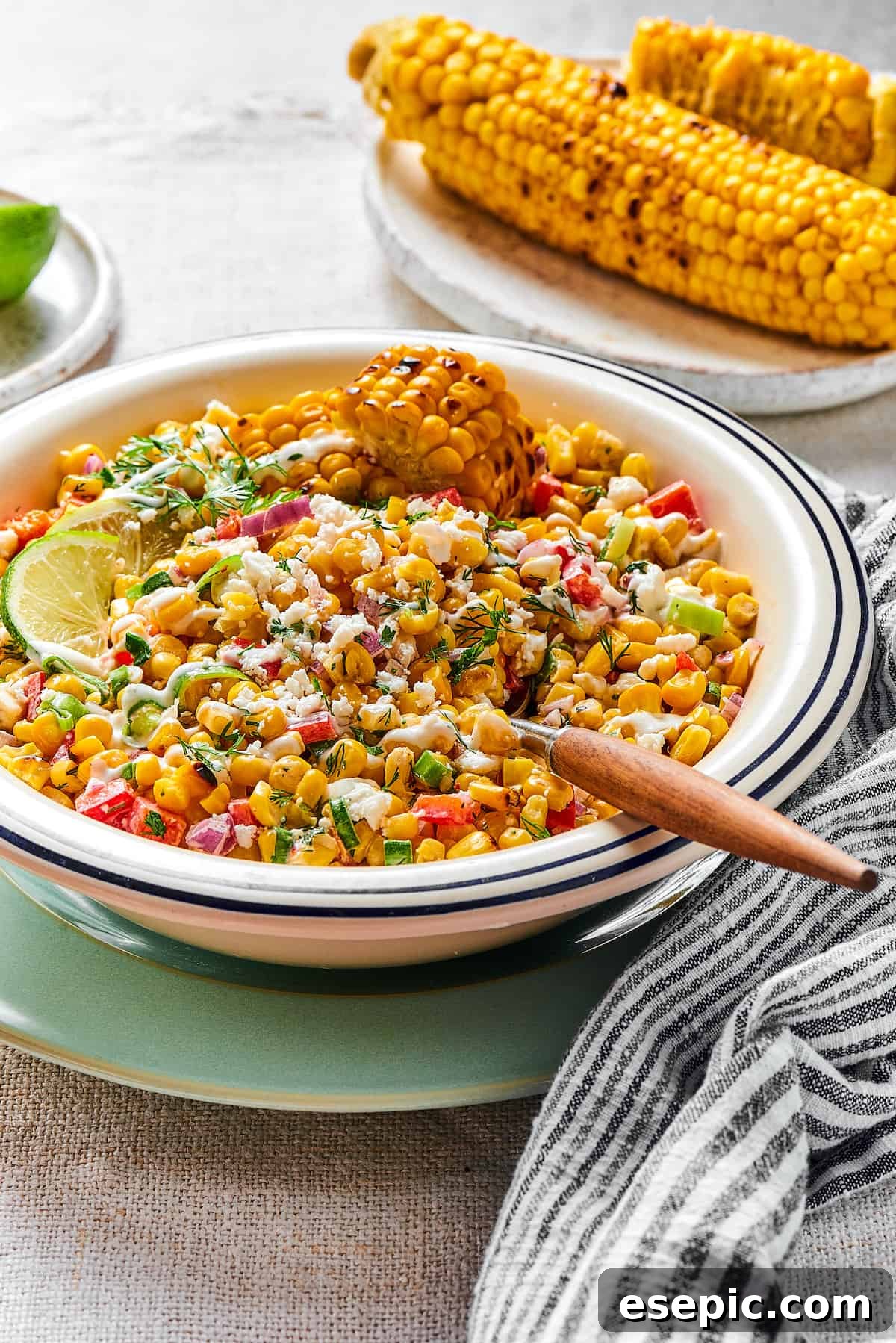 Mexican Street Corn Salad is a mouthwatering dish that’ll have everyone begging for the recipe! Fresh corn kernels in a killer creamy sauce. Elote salad in a bowl with a wooden-handled spoon.