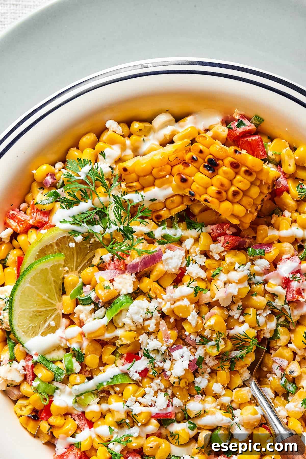 Mexican Street Corn Salad is a mouthwatering dish that’ll have everyone begging for the recipe! Fresh corn kernels in a killer creamy sauce. Close-up shot of grilled corn salad with creamy dressing, lime wedges, and chopped herbs.