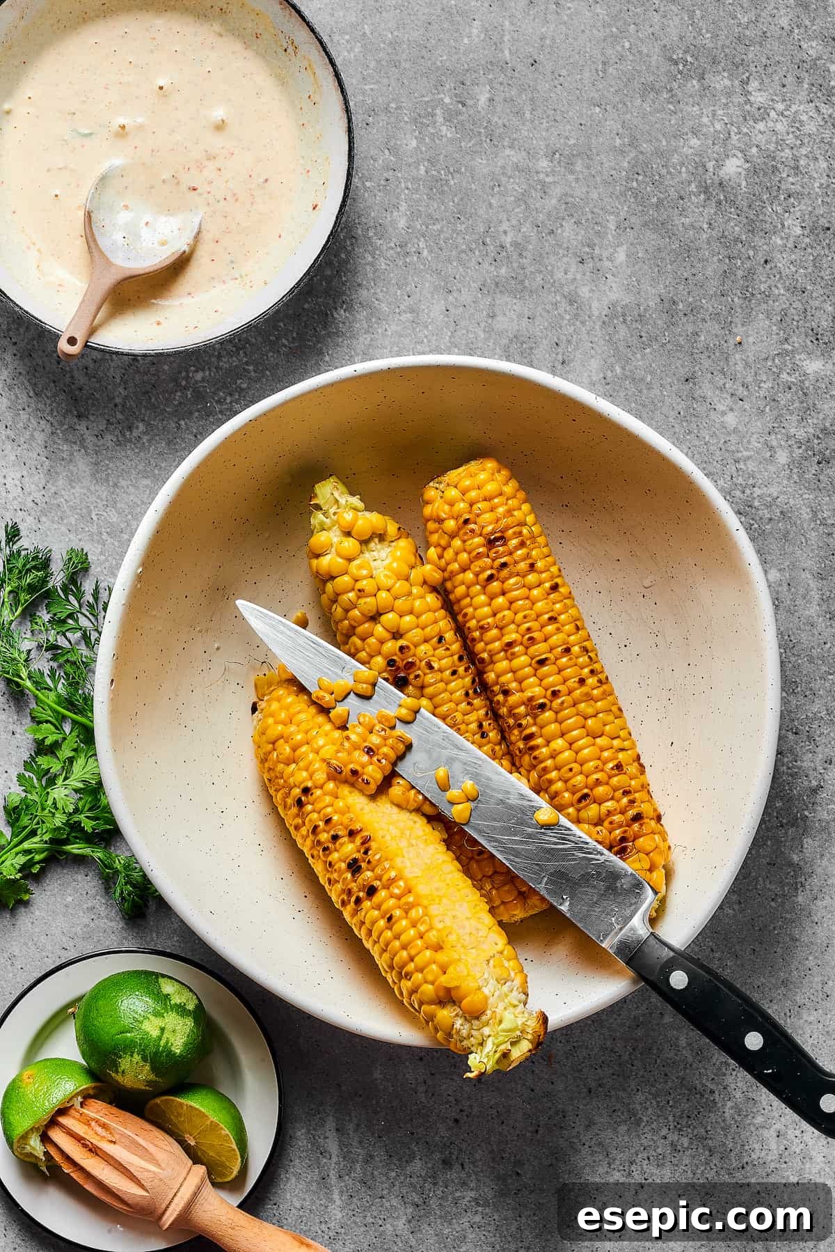 Mexican Street Corn Salad is a mouthwatering dish that’ll have everyone begging for the recipe! Fresh corn kernels in a killer creamy sauce. Grilled corn on the cob. Some of the kernels have been cut away from the corn cobs, and a knife is resting in the bowl.
