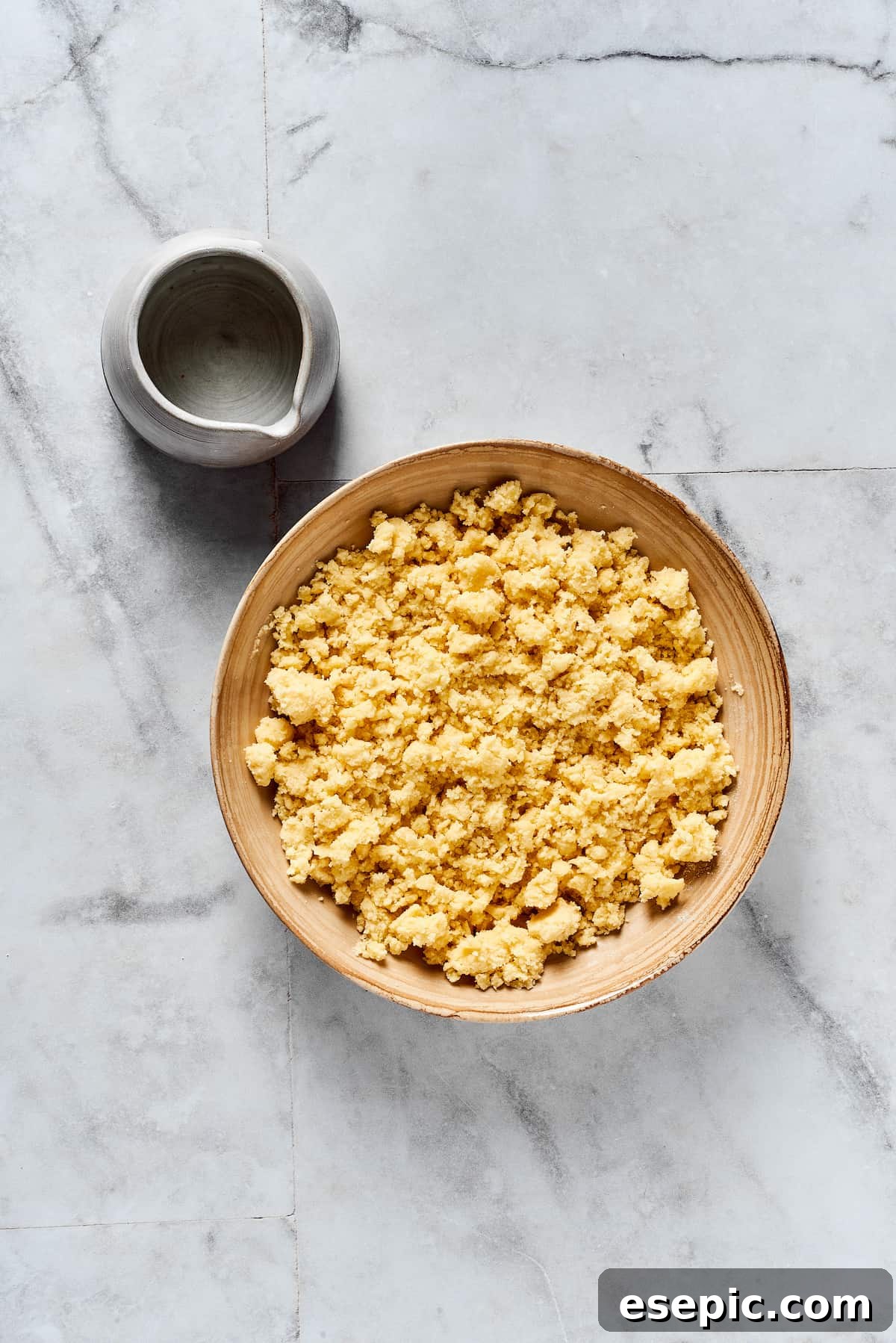 A close-up of crumbly pie dough in a mixing bowl, not yet pressed together, showing distinct pieces of butter.
