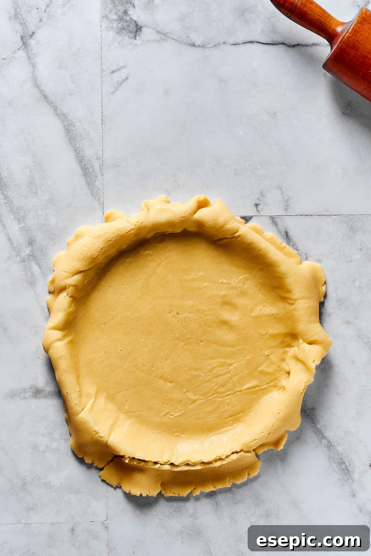 A rolled-out pie crust in a dish, with the edges overhanging the dish.