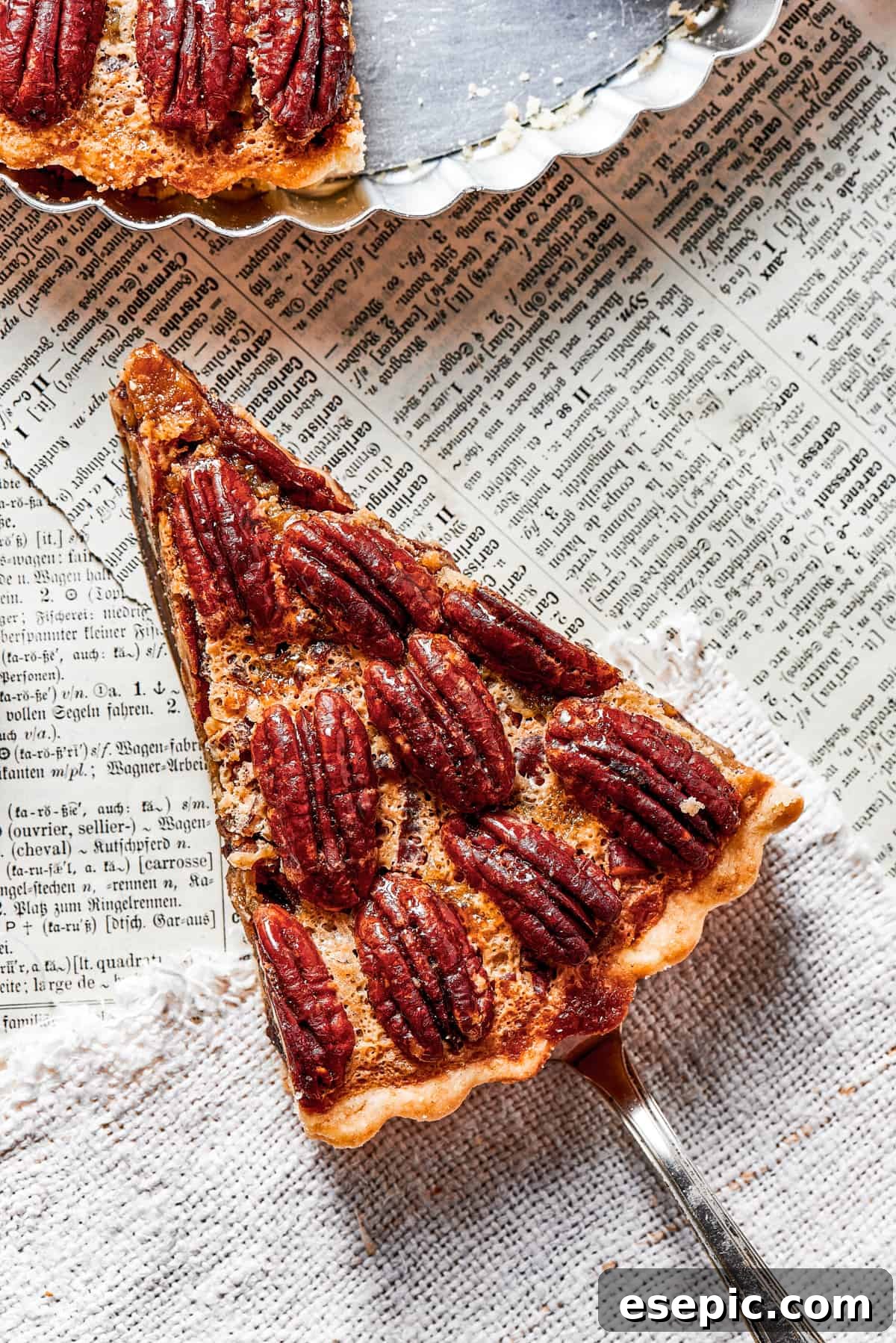 An overhead shot of a freshly baked slice of pecan pie held over a vintage newspaper, with the pie plate artfully blurred in the background, emphasizing its homemade charm.