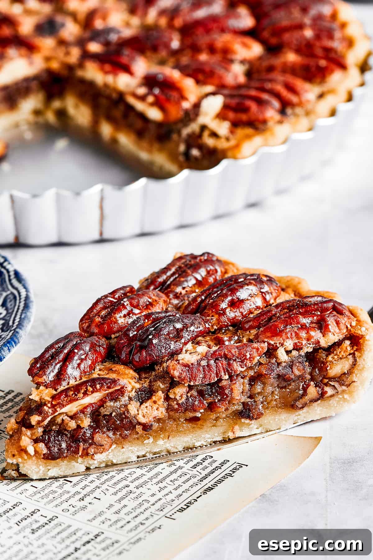A beautiful slice of pecan pie, rich with maple filling and toasted pecans, sits gracefully on a pie server, positioned beside the remaining pie in its dish.
