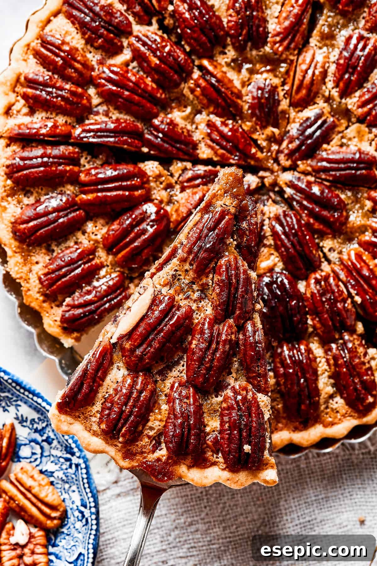 A close-up view of a generous slice of maple pecan pie being carefully lifted from a pie dish, showcasing its gooey filling and crunchy pecan topping.