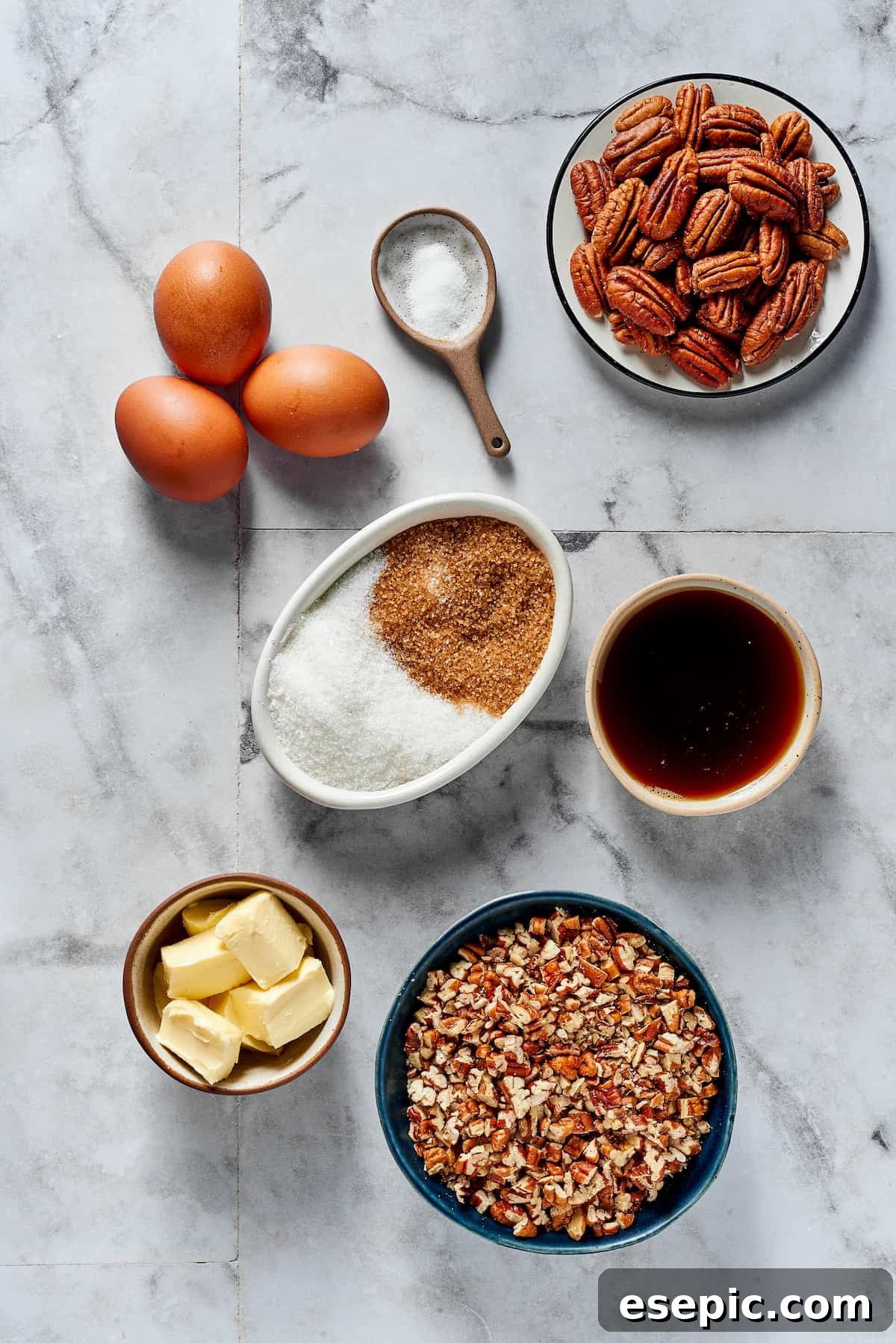 A flat lay of all the essential ingredients for pecan pie: fresh eggs, a pinch of salt, whole and chopped pecans, white and brown sugar, pure maple syrup, and cubes of unsalted butter.