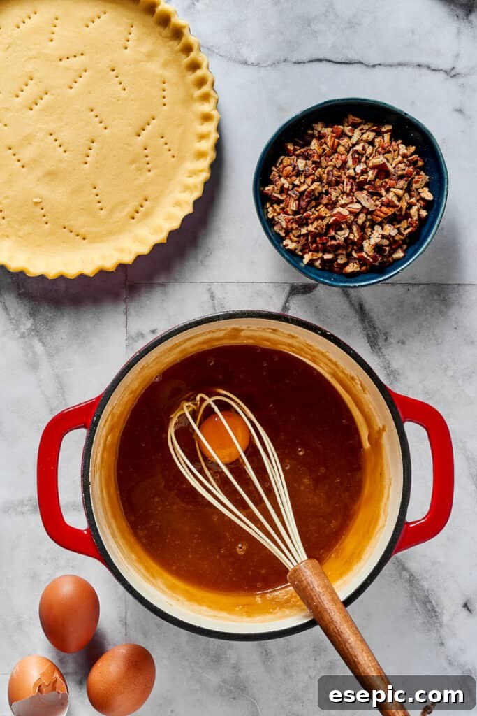Close-up shot of eggs being whisked into a cooled maple syrup mixture in a bowl, creating a smooth and glossy pecan pie filling.