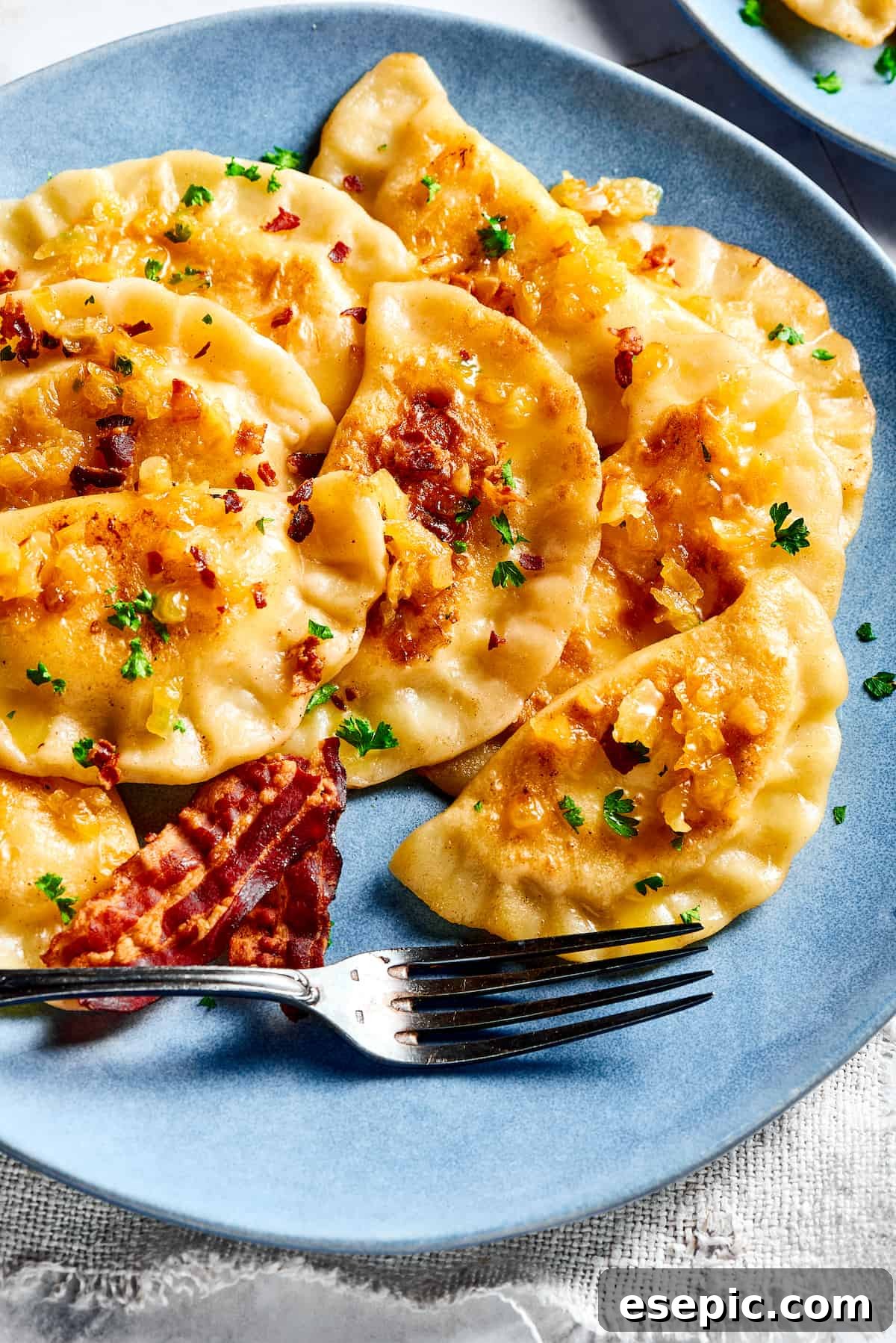 Classic Homemade Pierogi with Potato and Cheese, Crispy Bacon, and Caramelized Onions Delicious homemade potato and cheese pierogi ruskie topped with caramelized onions and crispy bacon bits, served on a rustic plate.
