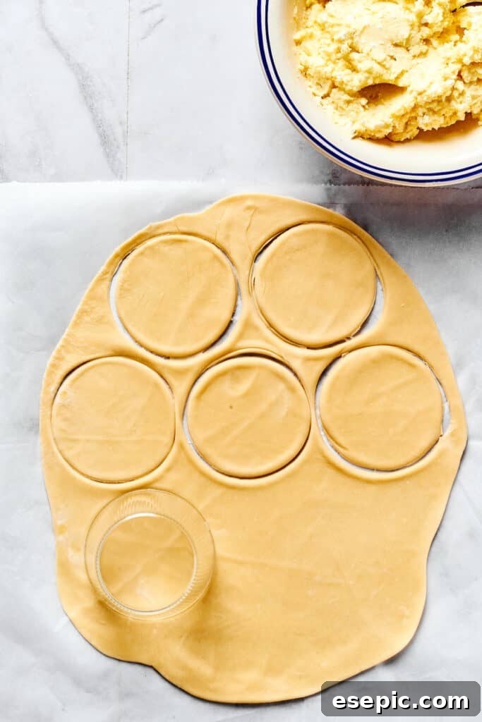 The Ultimate Homemade Pierogi Guide 6 Rolled out pierogi dough with circles cut out, next to a bowl of creamy potato and cheese filling on a floured surface.